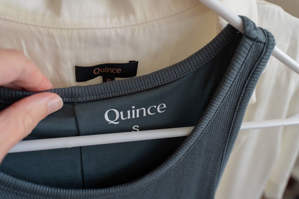 A close-up of a grey tank top on a clothing hanger, with a printed label reading "Quince" visible inside.
