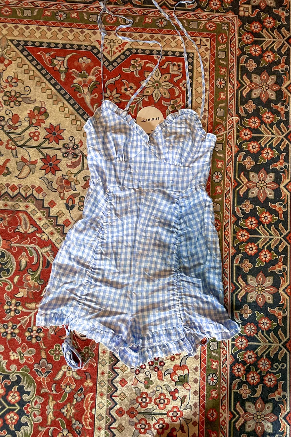 A blue and white gingham romper lying flat on a red, white, and blue oriental rug.