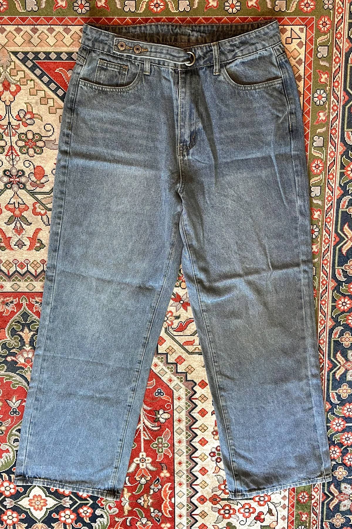 A pair of wide leg jeans lying flat on a red, white, and blue oriental rug.