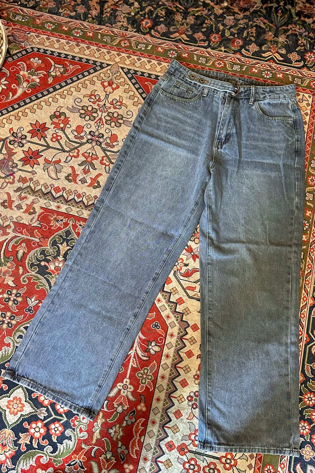 A pair of wide leg jeans lying flat on a red, white, and blue oriental rug.