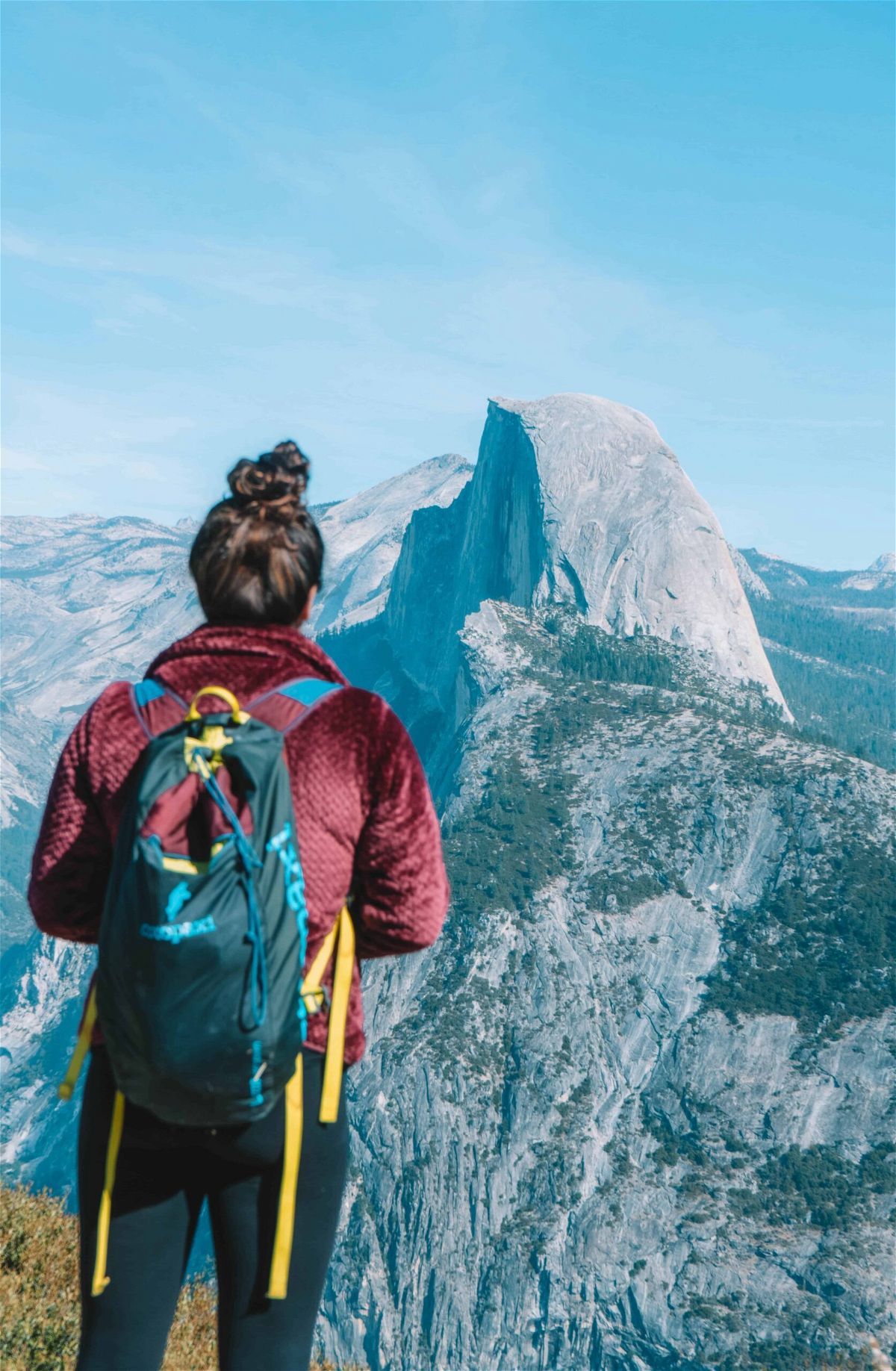A woman in a burgundy jacket looks out at Half Dome in Yosemite.