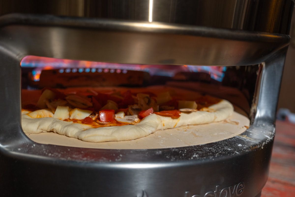A close-up of a raw pizza inside of a Pi Prime Pizza Oven with flames visible inside. 