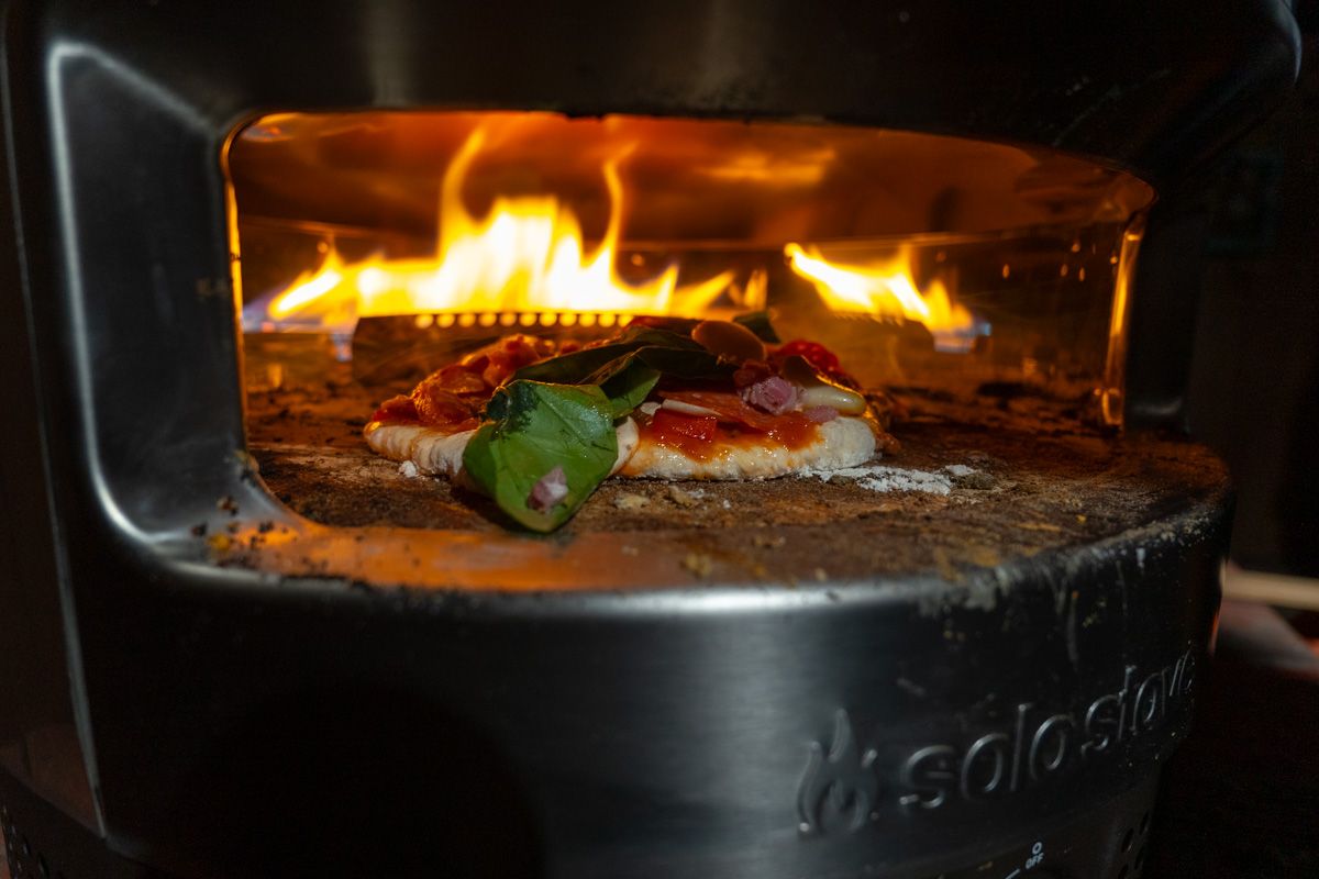 A close-up of a freshly cooked pizza inside of a Pi Prime Pizza Oven with flames visible inside. 