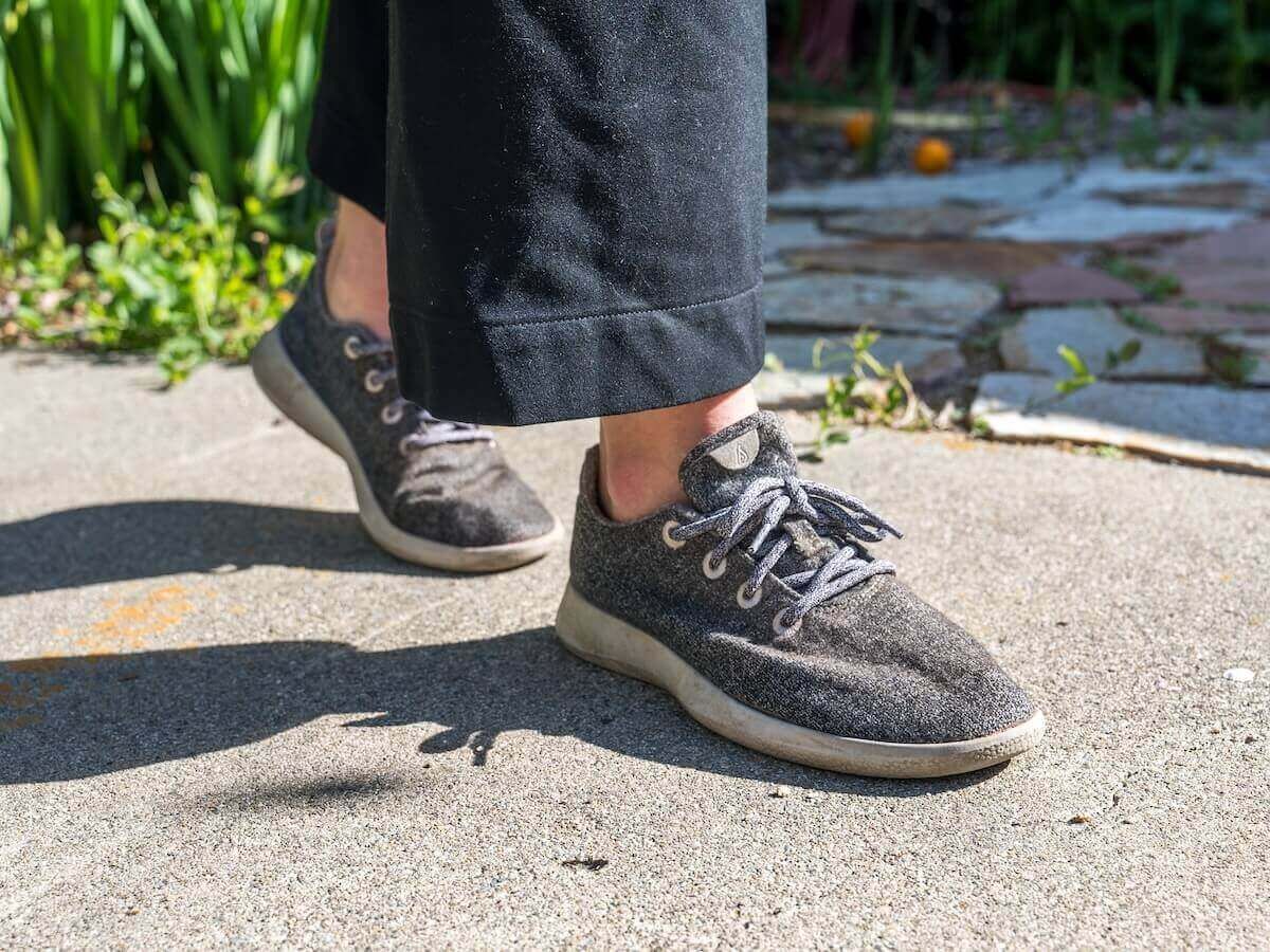 A pair of feet wearing grey sneakers walks along a garden path.
