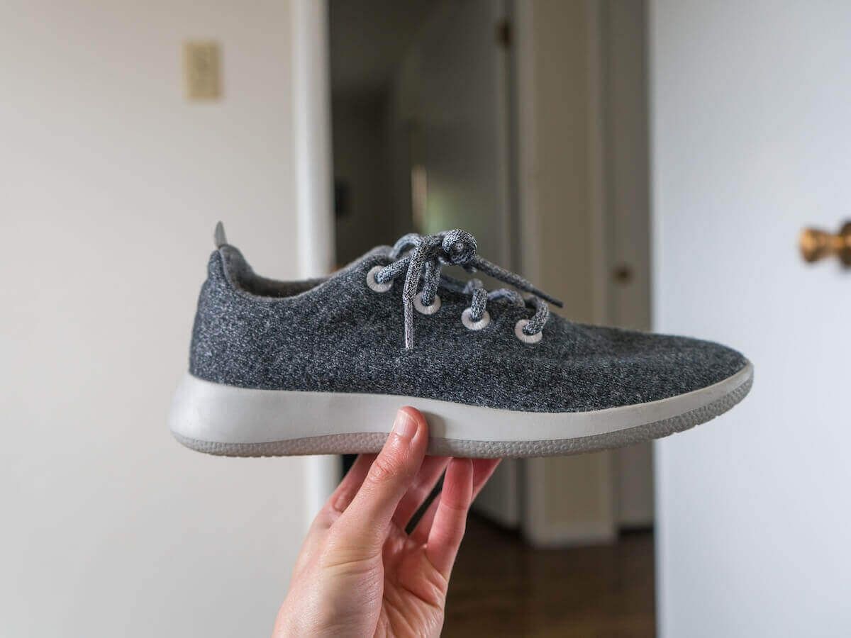 A hand holds up a a grey sneaker to examine for this Allbirds Wool Runners Review.