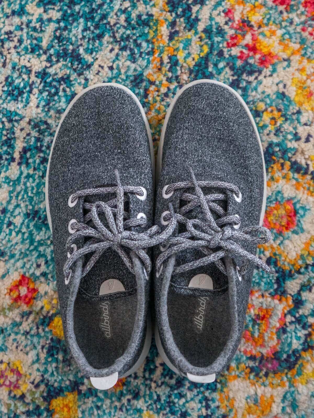 A pair of brand new grey sneakers seen from above, sitting on a patterned, multi-colored rug.