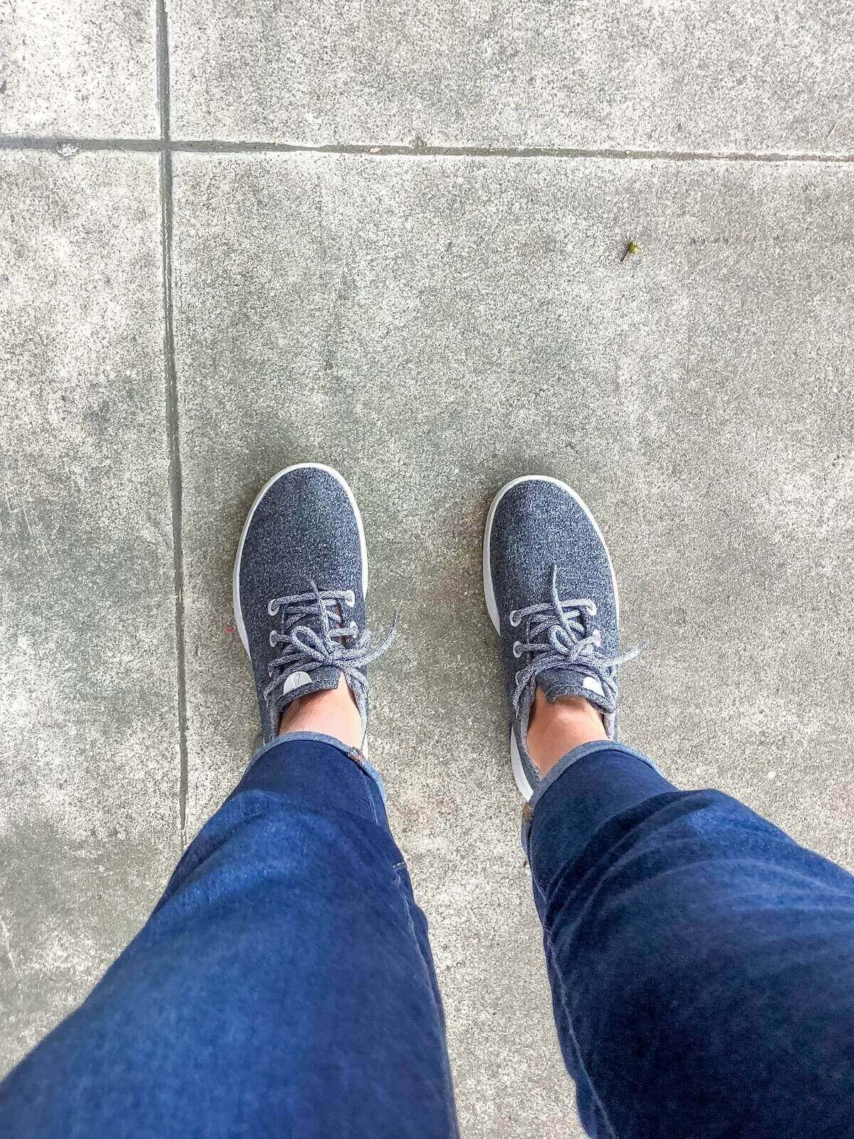A view looking down at a pair of feet wearing a pair of grey Allbirds Wool Runners.