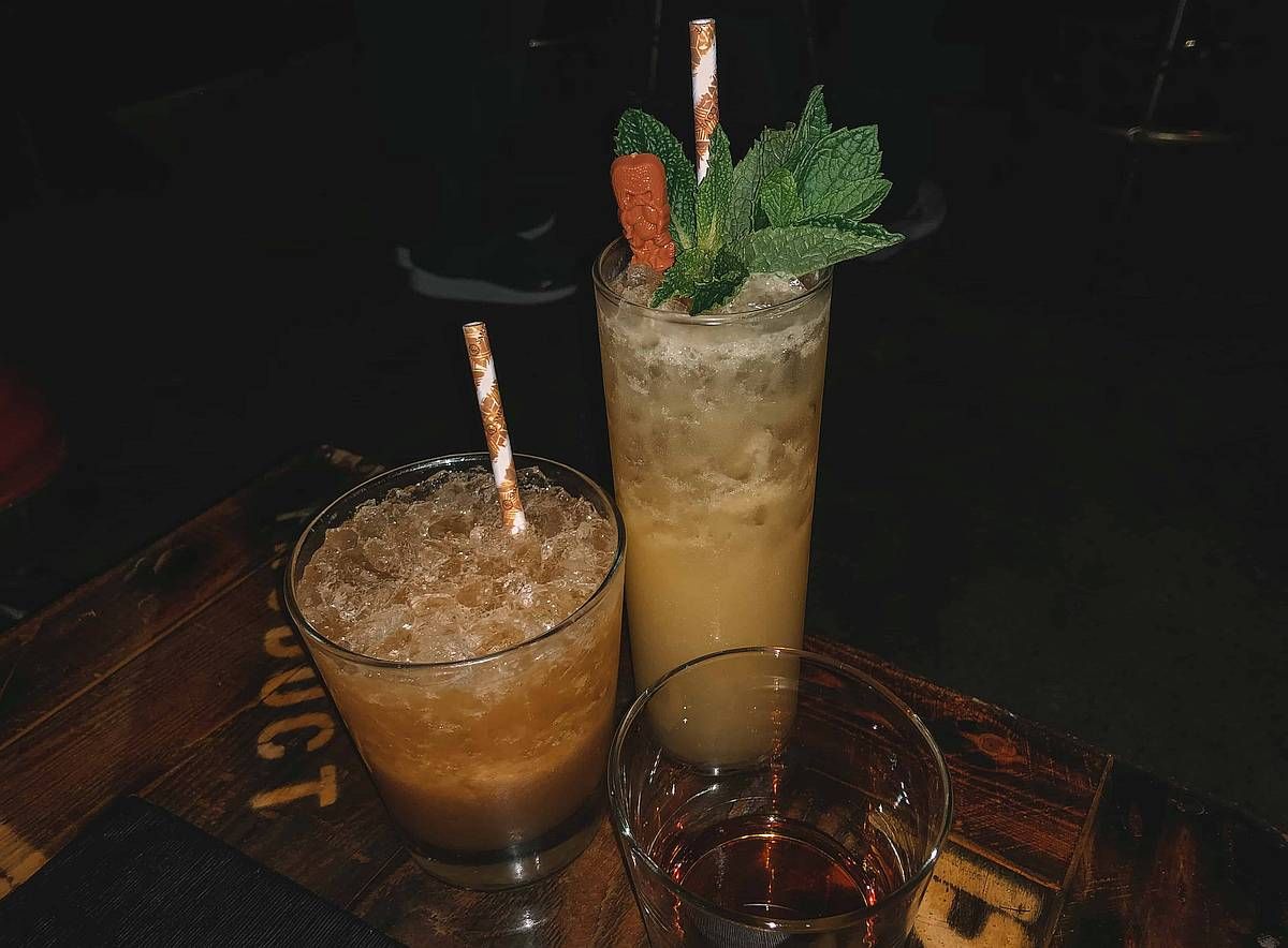 Two tropical cocktails sitting on a table in a dark bar.