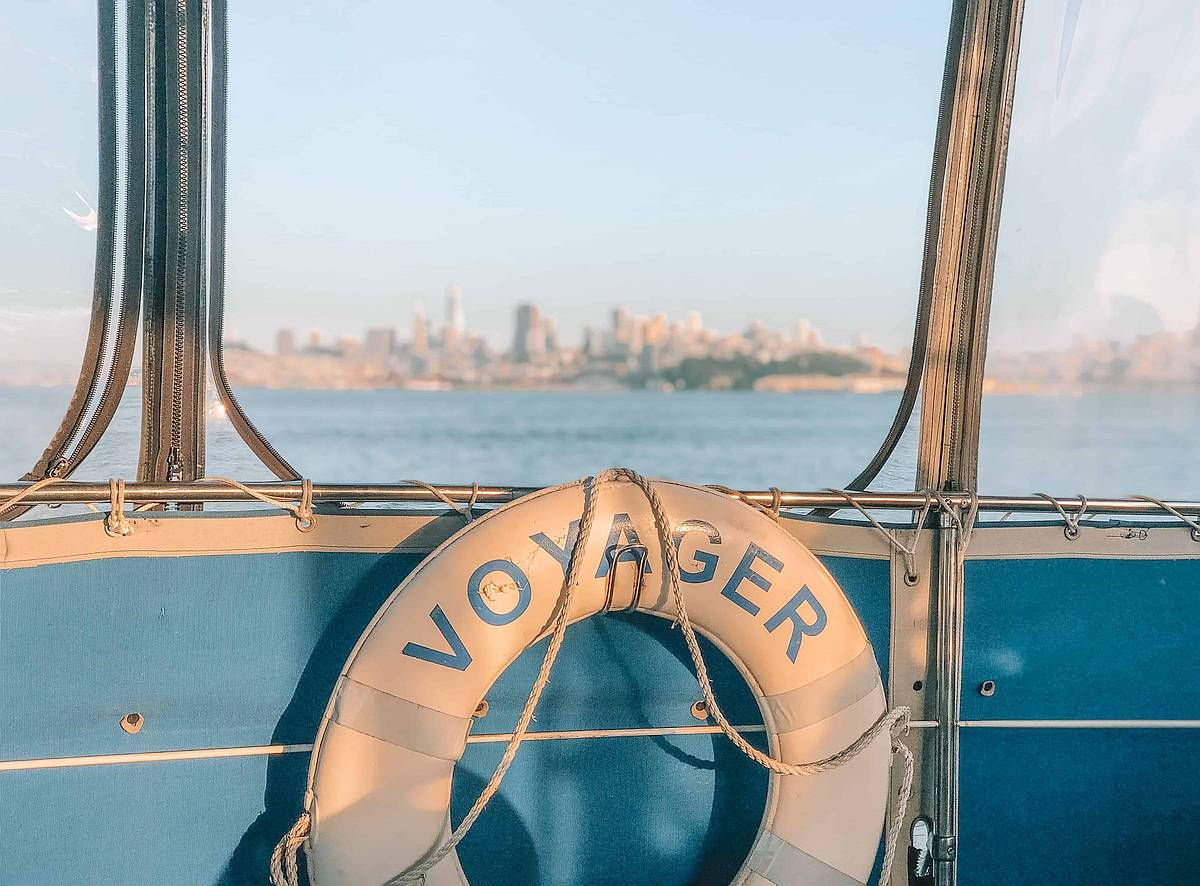 A view of white life-saver on the side of a blue boat, with the San Francisco skyline in the distance.