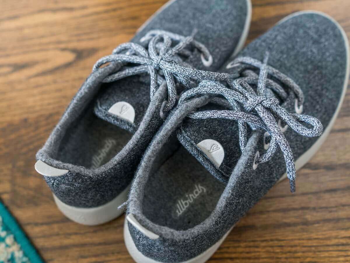 A pair of grey sneakers sits on a hardwood floor.