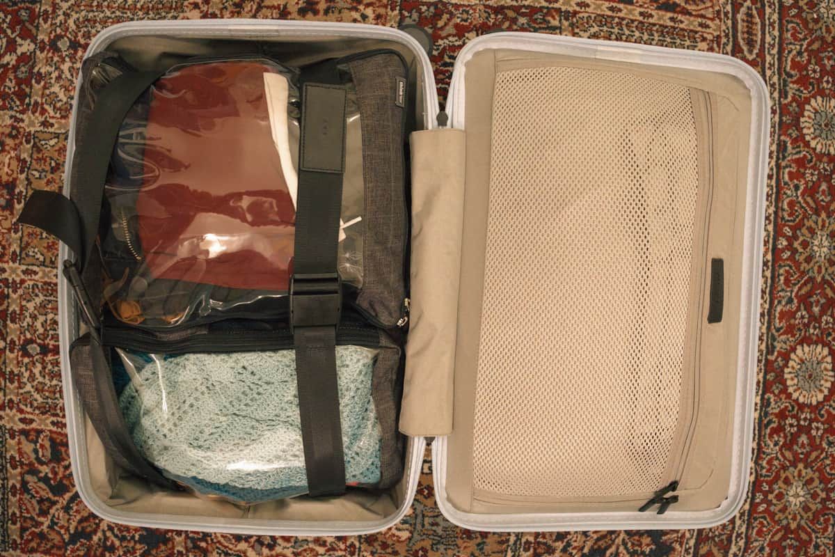 An open suitcase packed with clear packing cubes sitting on a red patterned rug.