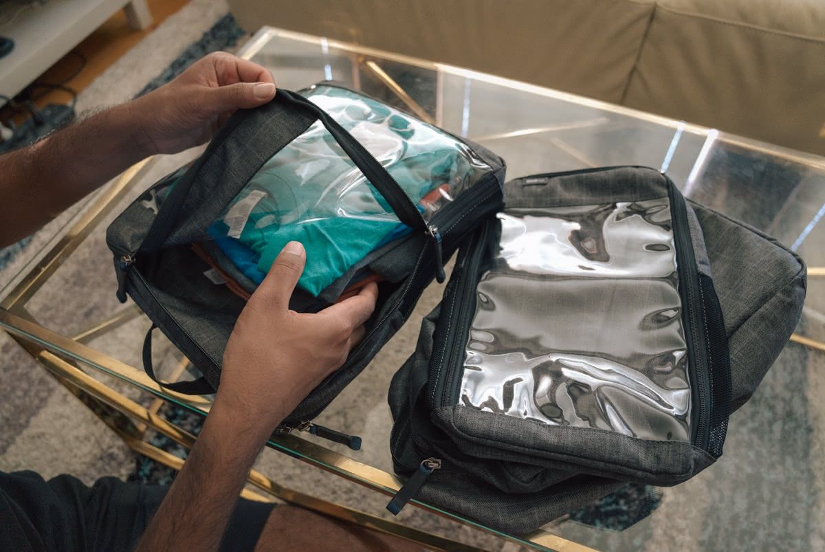 A pair of hands packing clothing into a clear packing cube sitting on a glass coffee table.
