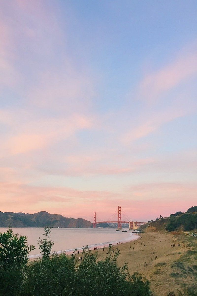 A view of a beach at sunset with the Golden Gate Bridge visible in the distance.