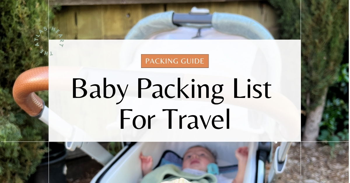 "Baby packing list for travel guide cover image showing baby in white stroller outdoors with green foliage background. White text overlay reads 'Baby Packing List For Travel' with orange 'PACKING GUIDE' label at top and 'THE ATLAS HEART' watermark on left side.
